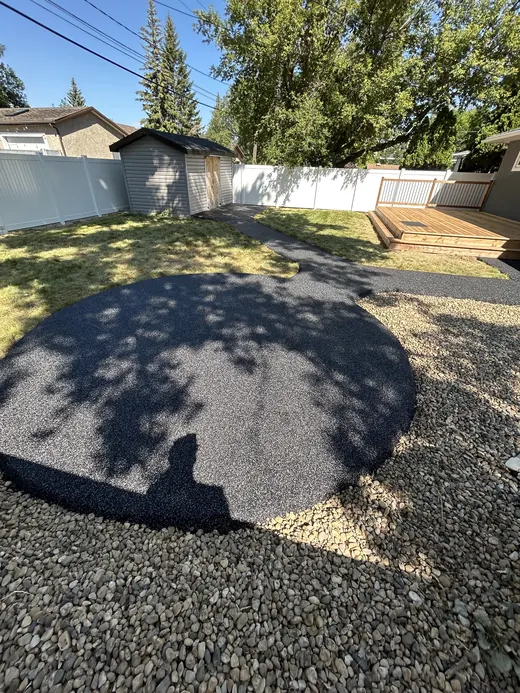 Circular black rubber patio pad in a backyard, bordered by river rock